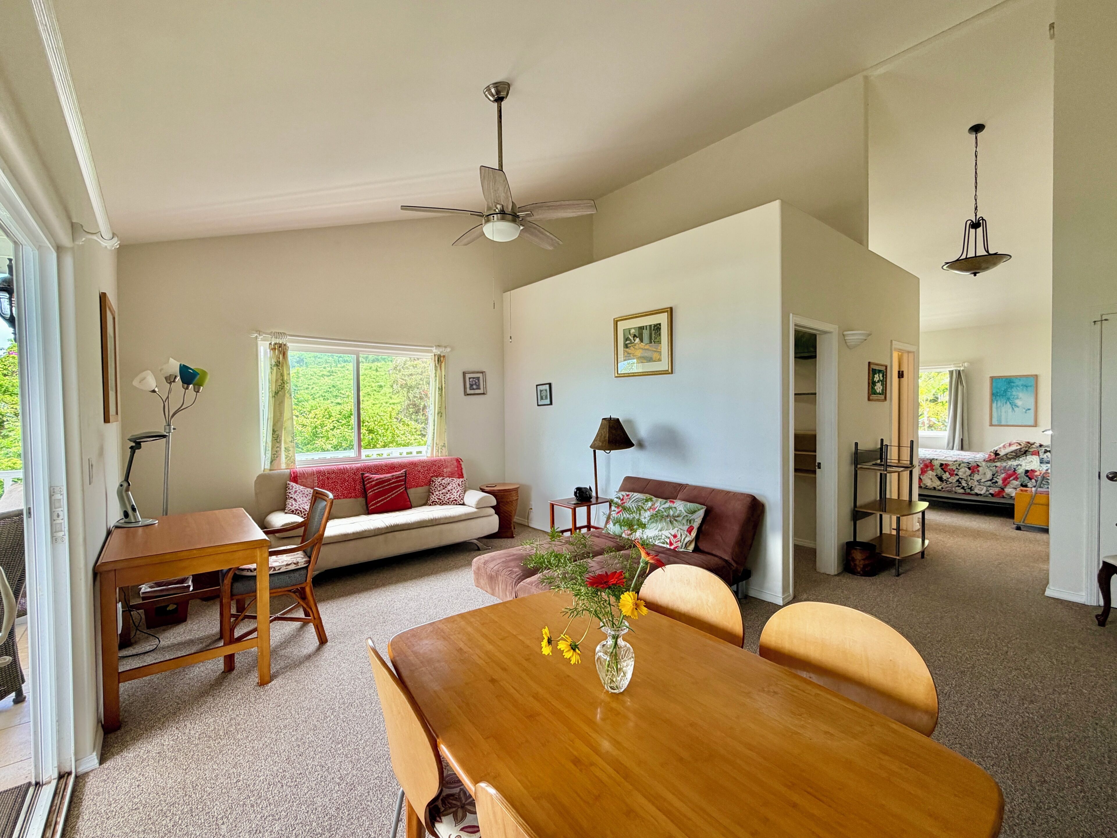 A spacious living room with a wooden dining table, a sofa, and a ceiling fan.