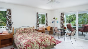A bedroom with a bed, a desk, and a chair, a balcony with chairs, and a ceiling fan.