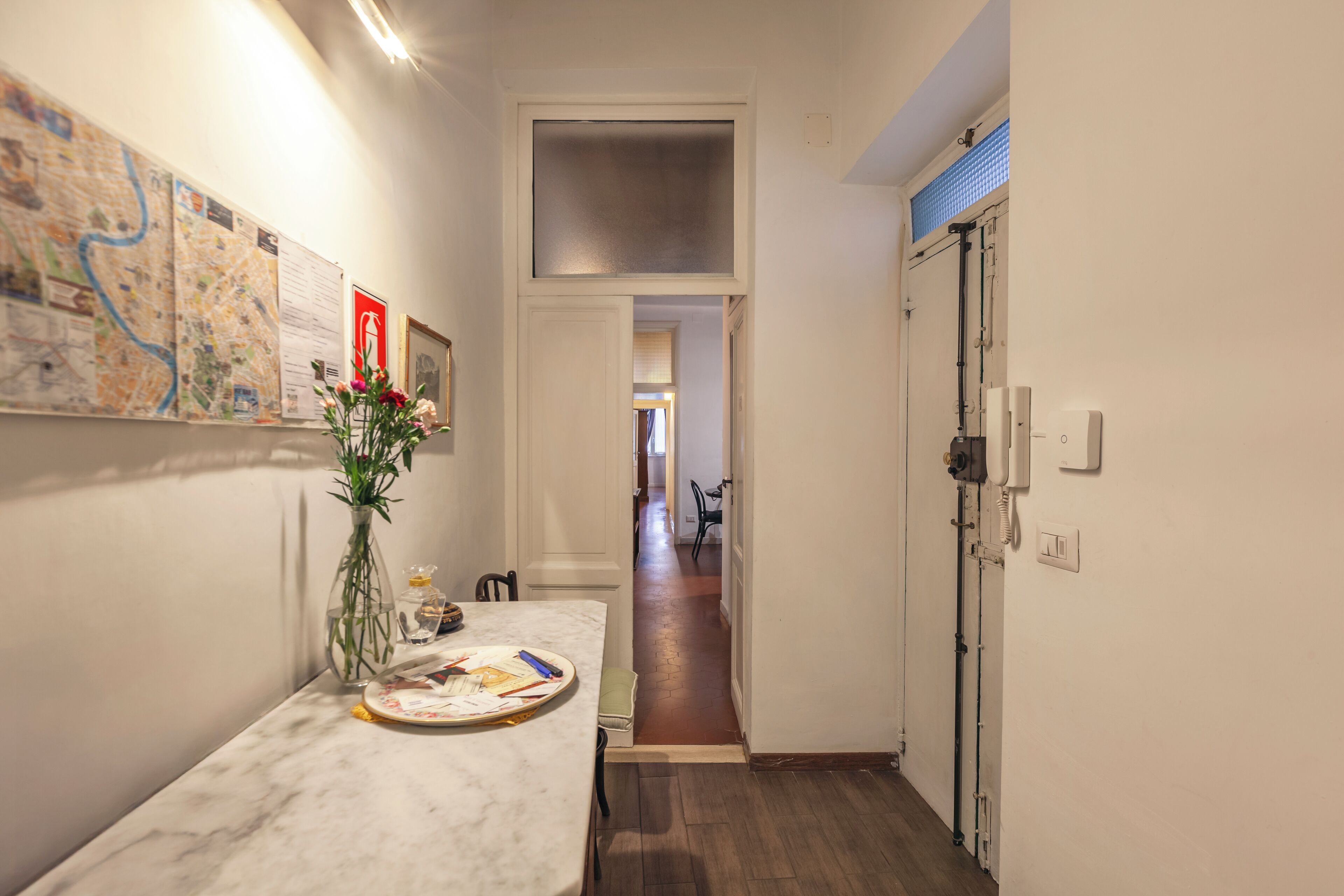 A narrow hallway with a marble table, a vase with flowers, and a map on the wall.