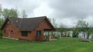 A wooden cabin with a porch and a view of a lake.