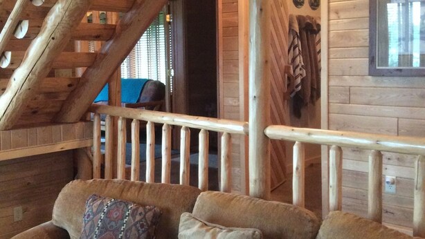 A wooden interior with a staircase, a cushioned sofa, and a wooden railing.