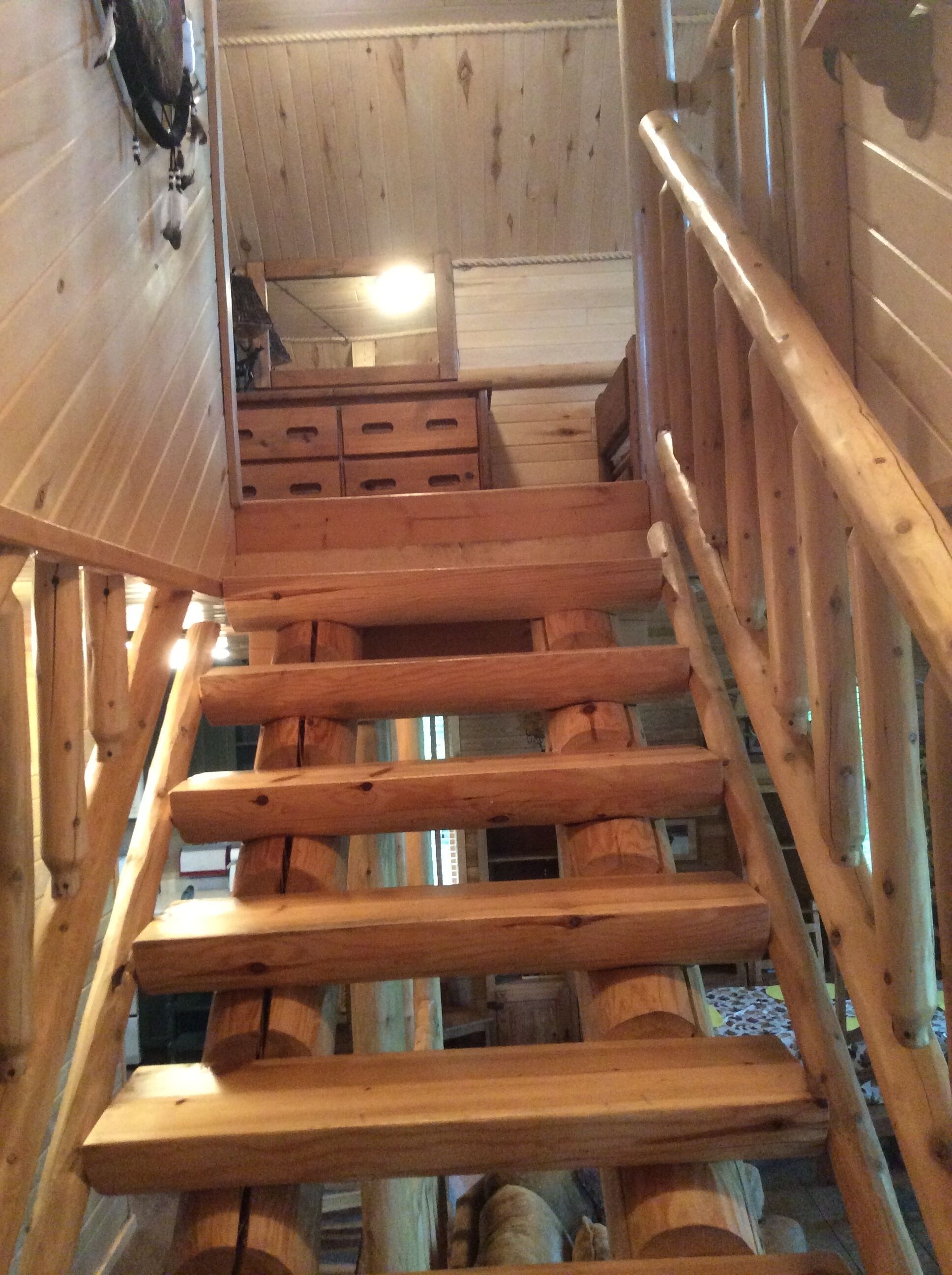 A wooden staircase with a handrail, leading to a room with a wooden ceiling and a window.