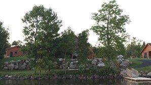 A lakeside cabin with a wooden deck, surrounded by trees and rocks.