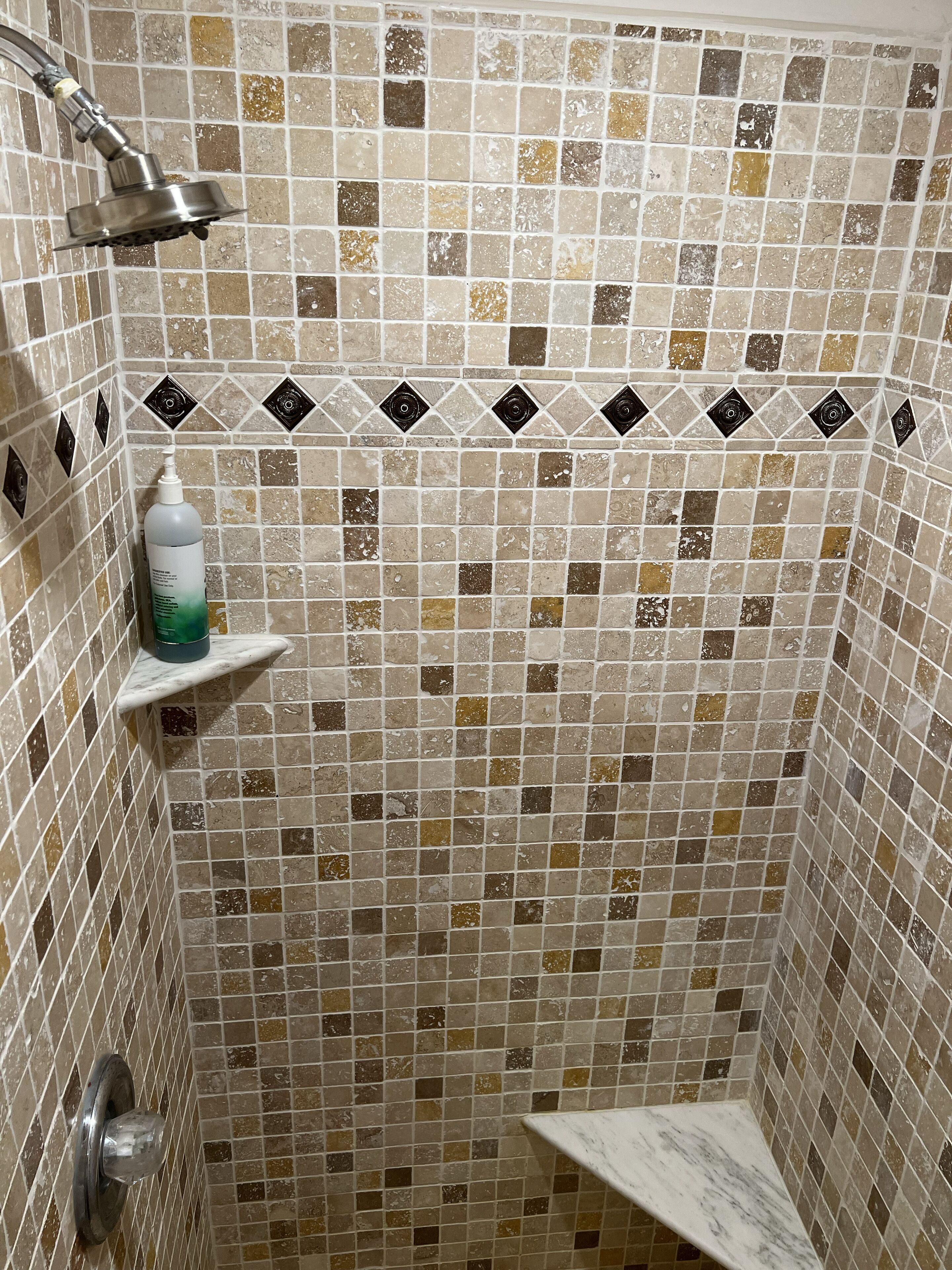 A shower with a tiled wall, a handheld showerhead, a soap dispenser, and a marble shelf.