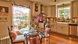 A kitchen with white cabinets, a gas stove, and a dishwasher. There is a dining table with chairs and a window with a view of trees. - On The Beach! Elegant Waterfront Manor 'The Pearl on Oyster Bay (Bremerton)