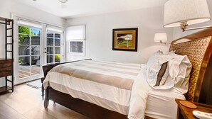 Une chambre à coucher comprenant un lit, une table de chevet, une lampe, un ventilateur de plafond, une fenêtre et une porte donnant sur un balcon.