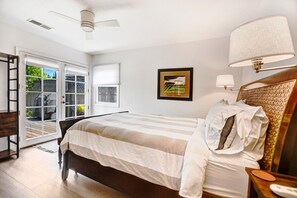 A bedroom with a bed, a nightstand, a lamp, a ceiling fan, a window, and a door leading to a balcony.