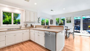 Une cuisine moderne avec des meubles blancs, un lave-vaisselle et un coin repas comprenant une table et des chaises.