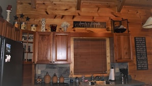 Une cuisine de style rustique, avec des meubles en bois, un pare-feu en pierre et une pancarte sur laquelle on peut lire : « C’est ici que la famille et les amis se réunissent. »