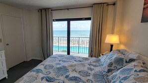 Ein Hotelzimmer mit einem Bett, einer Kommode, einer Lampe, einem Fenster mit Blick auf den Strand und das Meer sowie einem Bild an der Wand.