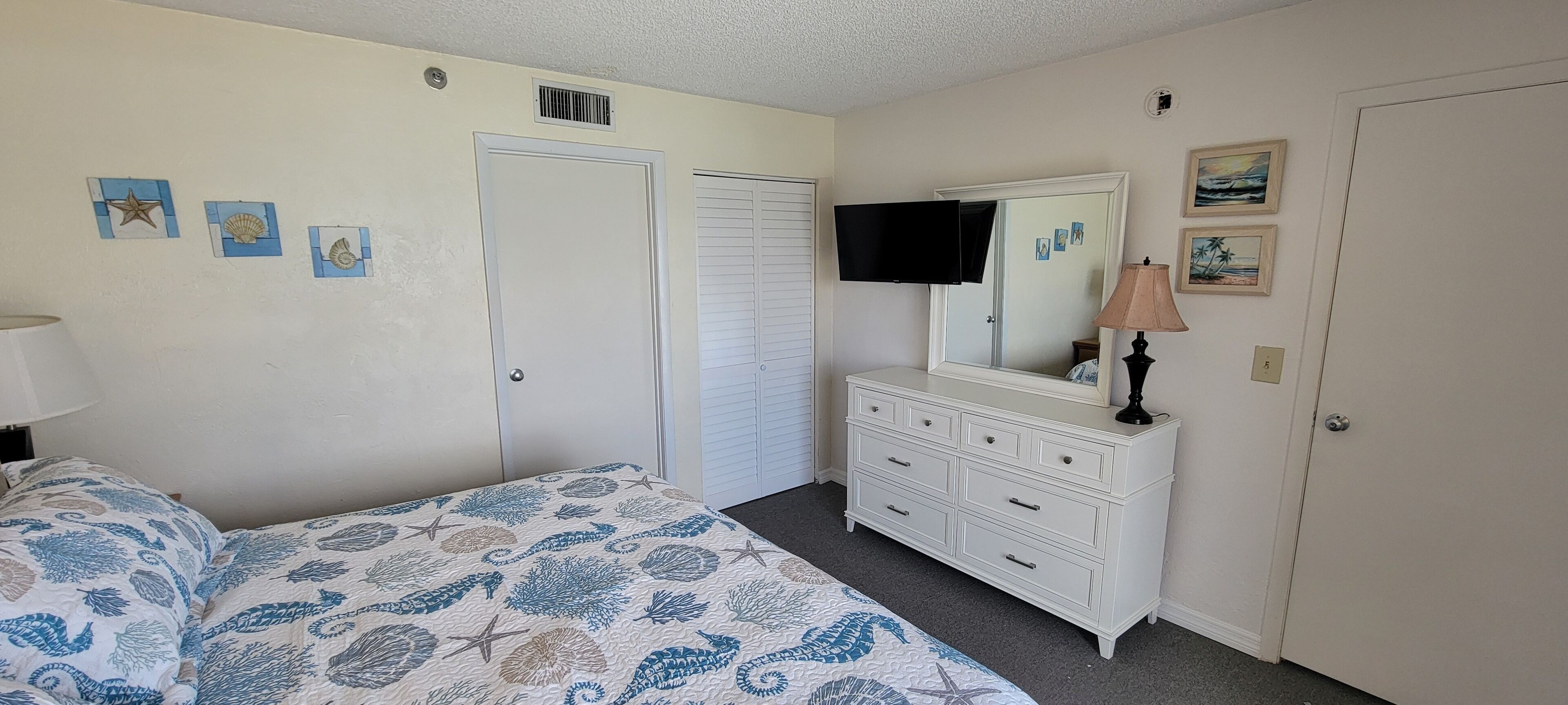 A bedroom with a bed, dresser, TV, and artwork on the wall.