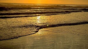 Ein Strand bei Sonnenuntergang mit Wellen und wolkenlosem Himmel.