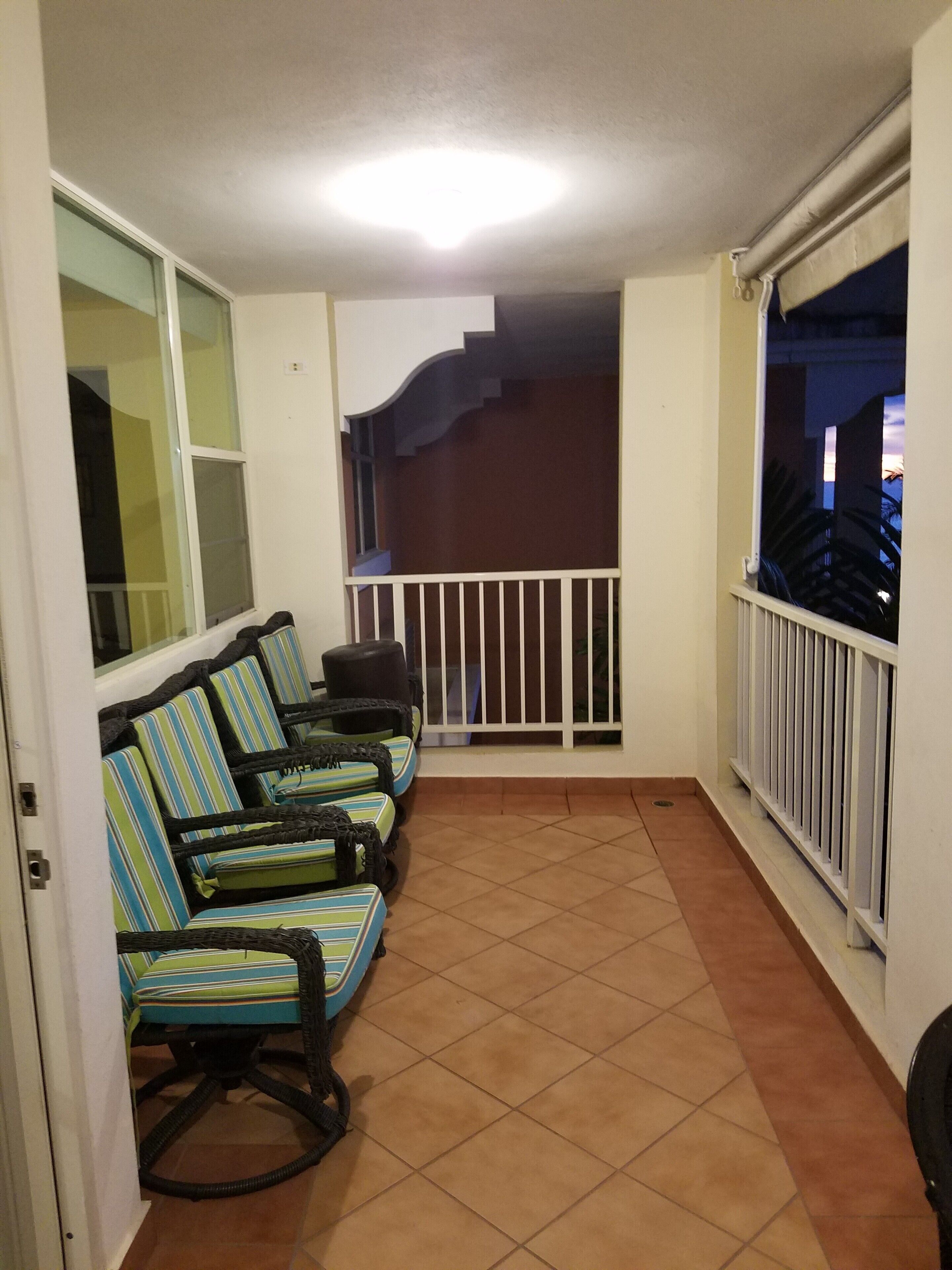 Un balcon avec quatre chaises à rayures, une balustrade blanche et une vue sur le ciel nocturne.