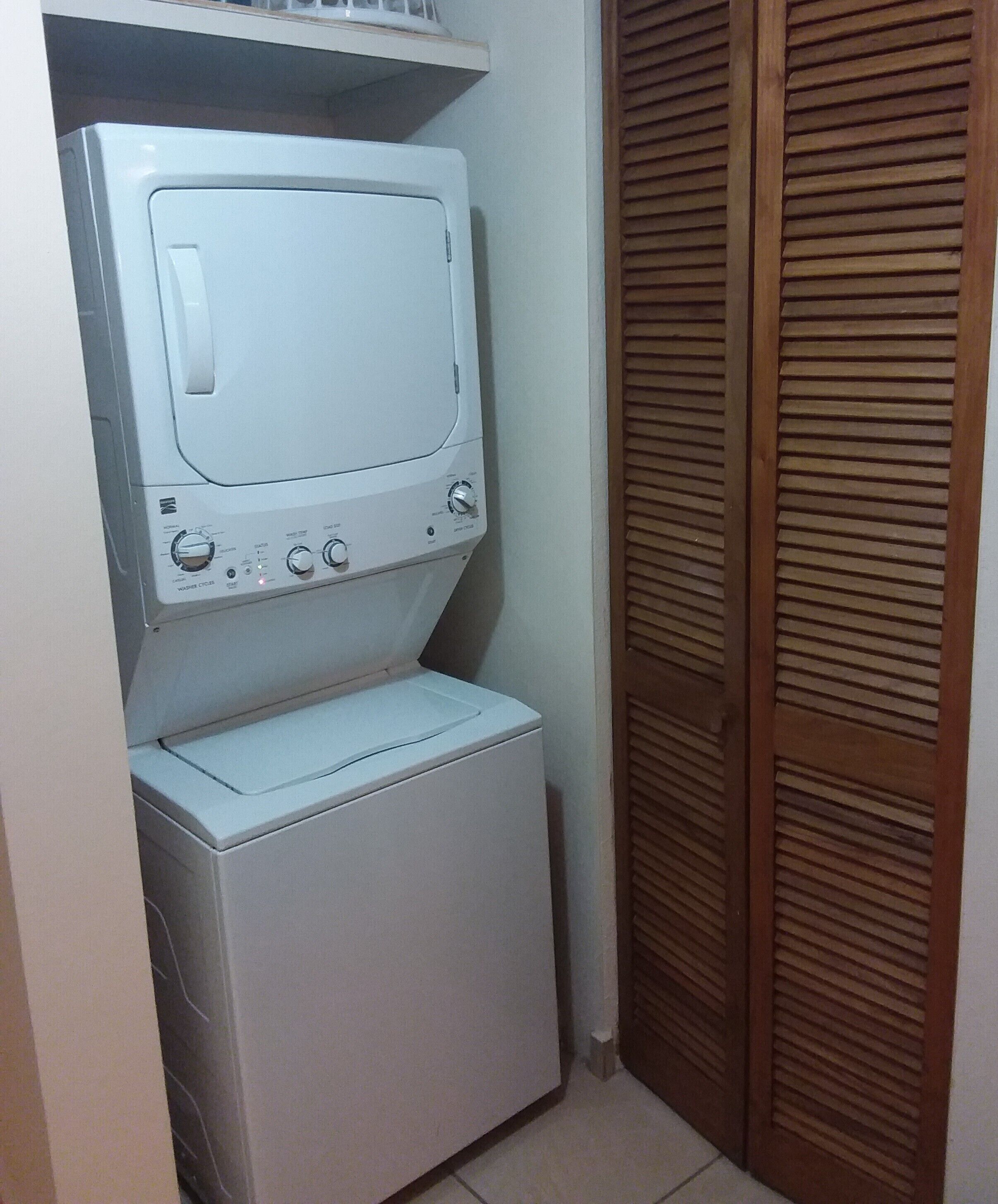 Une petite buanderie où la machine à laver et le sèche-linge sont placés l’un au-dessus de l’autre.