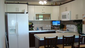 Una cocina con refrigerador, microondas y televisor en la pared.