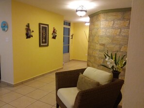 Un salon avec un canapé en osier marron, un mur décoratif en pierre et une porte donnant sur une autre pièce.