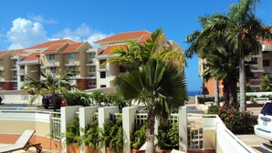 Un resort con edificios de varios pisos, palmeras y una zona de piscina con sillones de descanso.