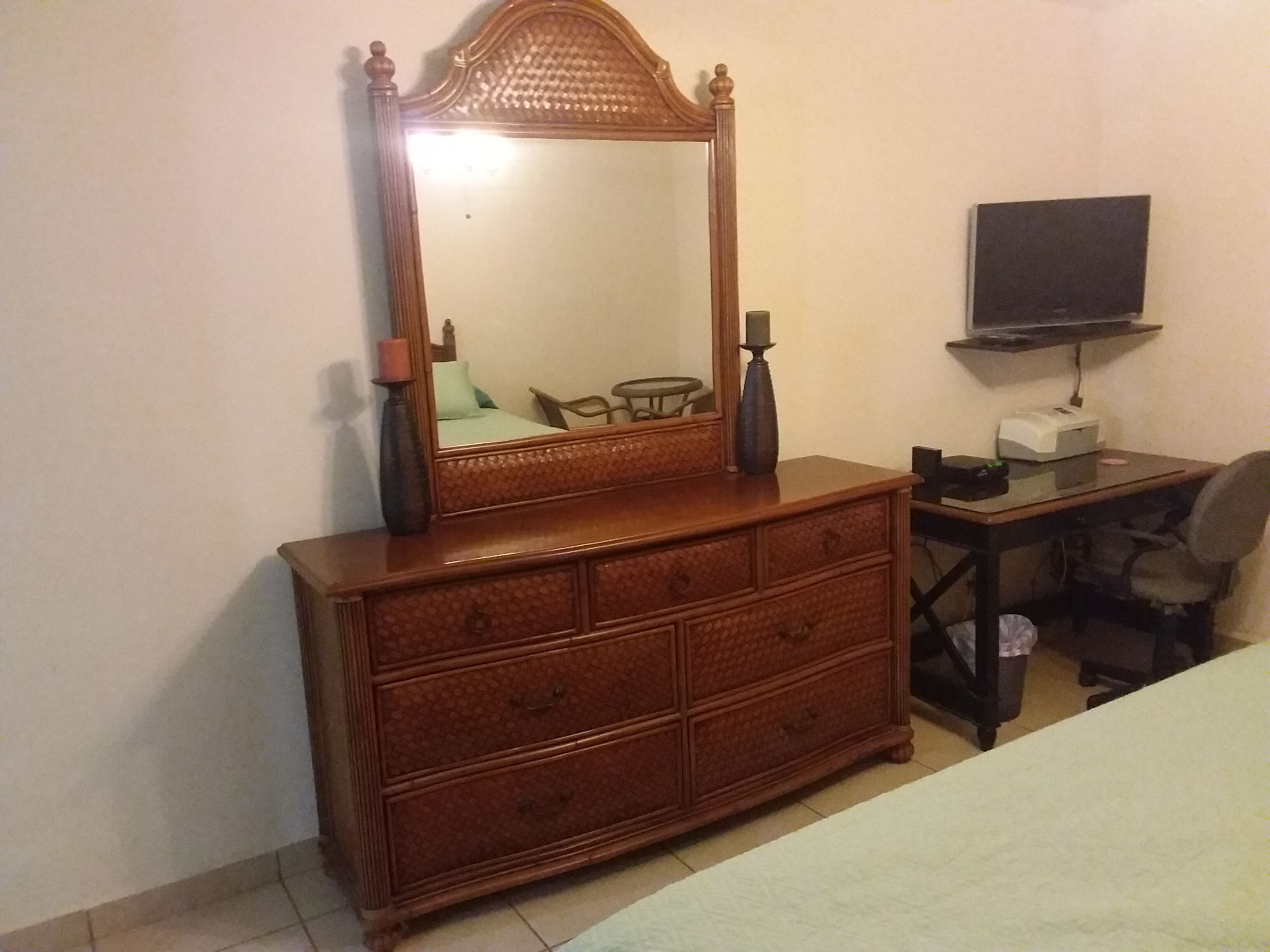 Un aparador de madera con espejo, un televisor sobre un soporte y un escritorio con una silla.