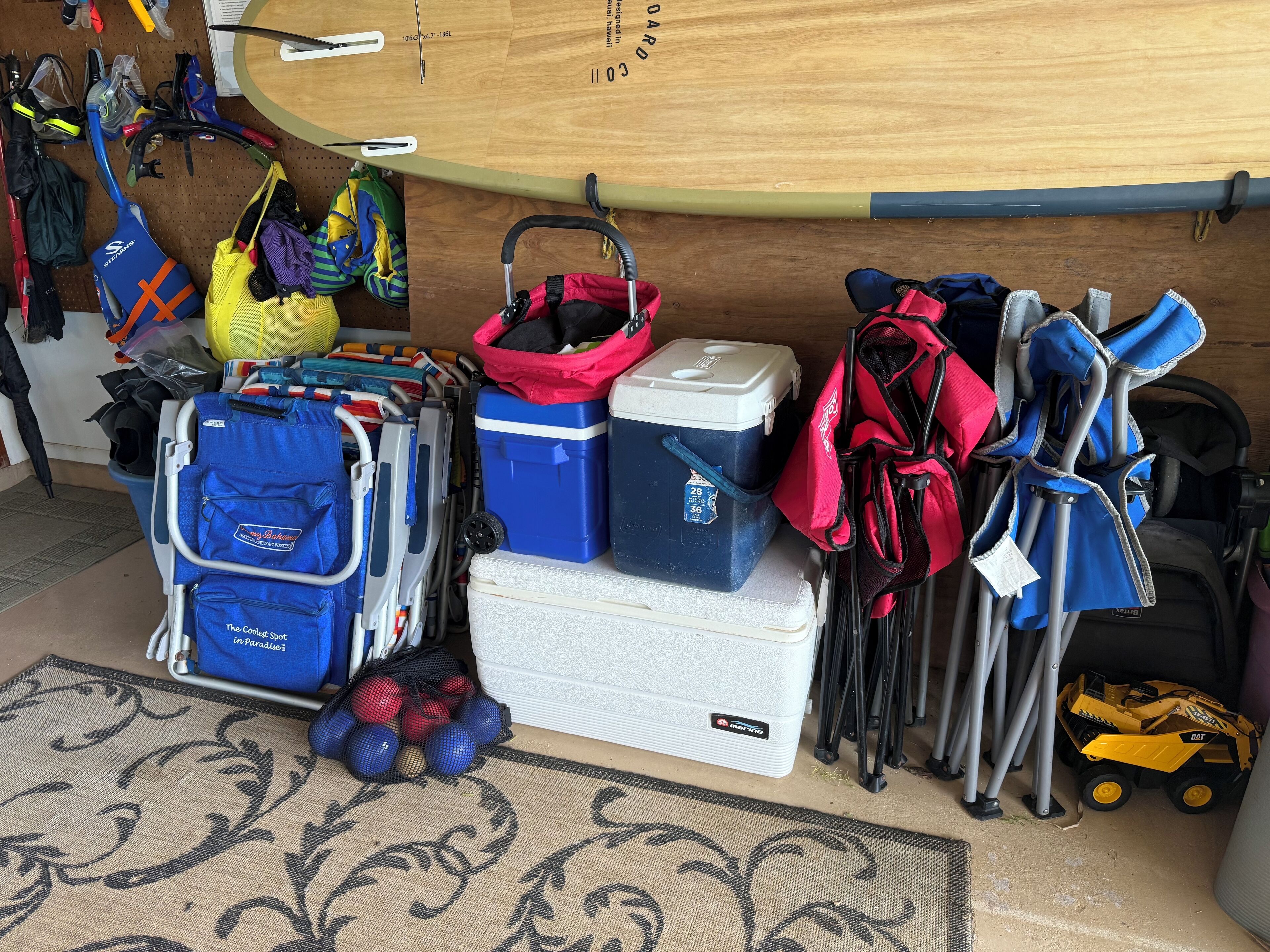 A storage area with various bags, coolers, and a surfboard.