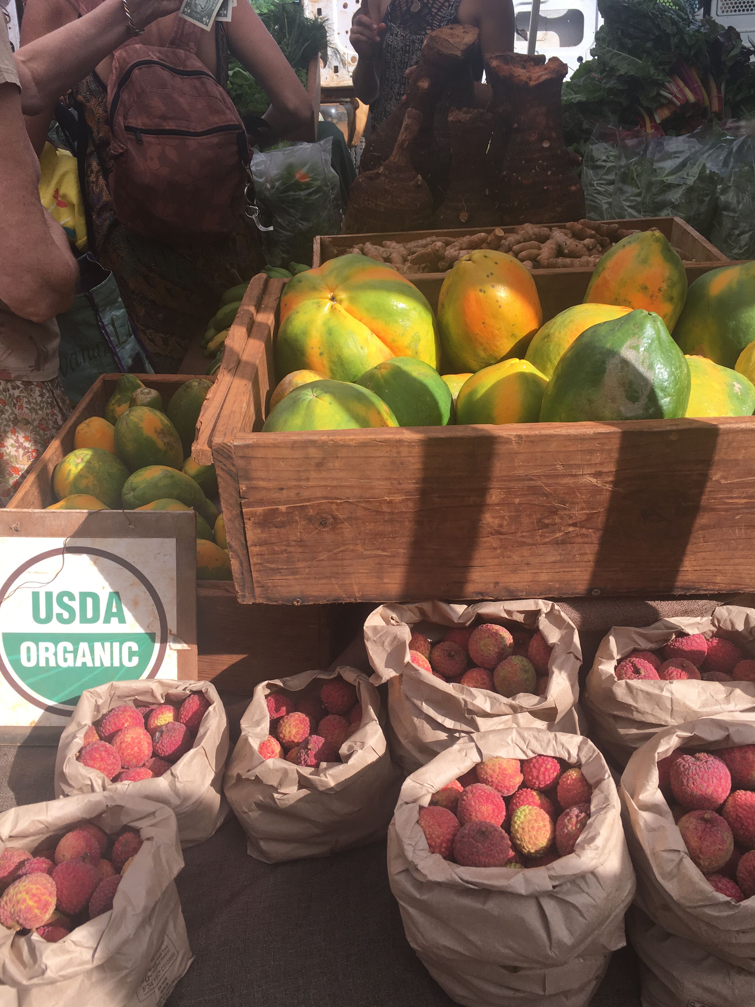 A market stall with USDA organic labeled boxes of mangoes and lychees.