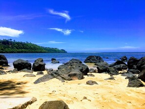 A beach with large rocks in the foreground and a clear blue sky.
