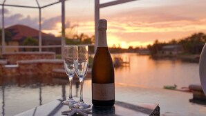 Une bouteille de vin et deux verres sur une table, près d’une étendue d’eau, avec une vue sur le coucher de soleil.