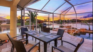 Un espace extérieur abrité où l’on peut prendre ses repas, avec vue sur une piscine et sur le coucher de soleil.