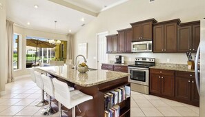 A spacious kitchen with dark wooden cabinets, a large island with bar stools, a built-in oven, and a microwave.