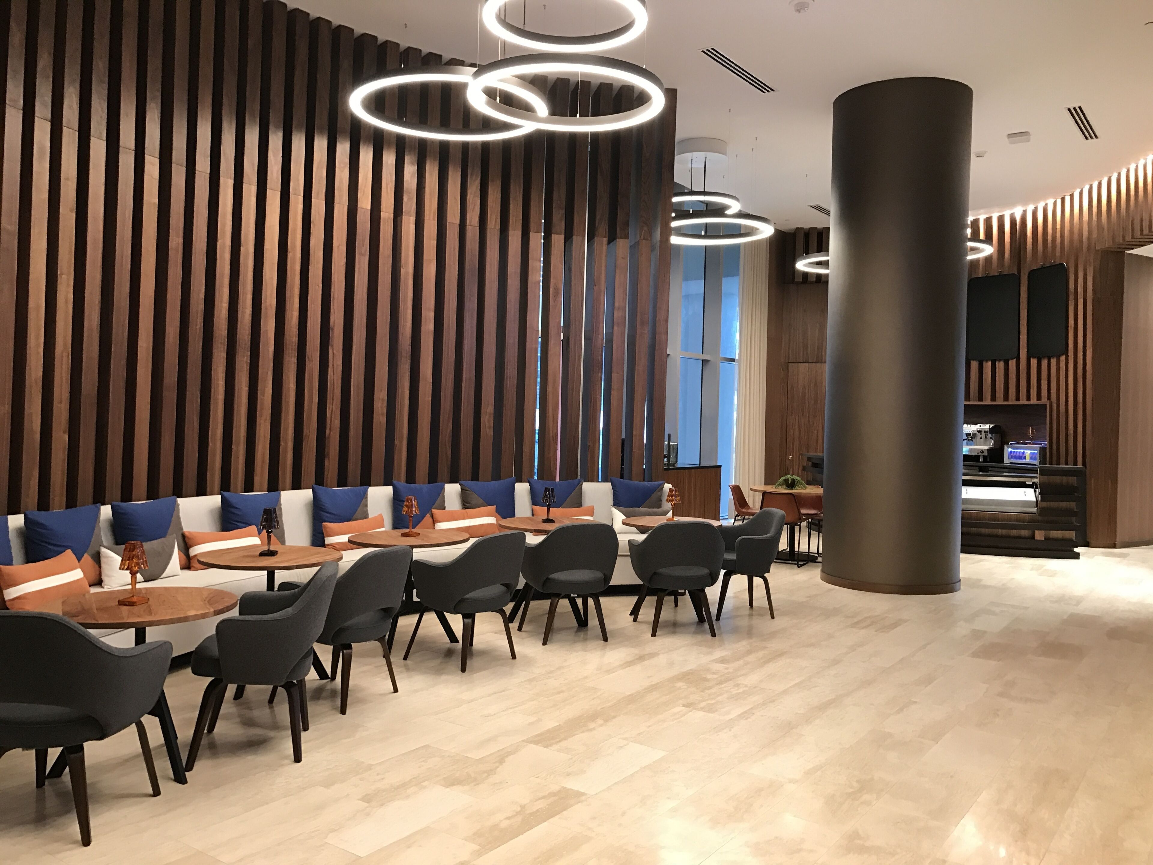 A modern interior with a long dining table, multiple chairs, and a high ceiling with circular light fixtures.