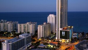Un hôtel de grande hauteur, avec de nombreux étages, un grand panneau publicitaire bien visible et une vue sur l’océan.