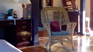 A room with a wicker chair, a desk with drawers, a lamp, and a patterned rug. - Contemporary farmhouse in Redwood National Park (Orick)