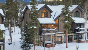 Ein großes, mehrstöckiges Chalet mit Steinaußenwand und Holzelementen, umgeben von schneebedeckten Bäumen und einem Berg im Hintergrund.
