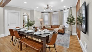 A modern living room with a dining area, wooden floors, and a large flat-screen TV.