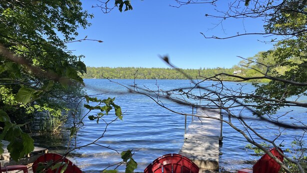 Blick auf einen See mit roten Stühlen und einem Steg, der ins Wasser führt.