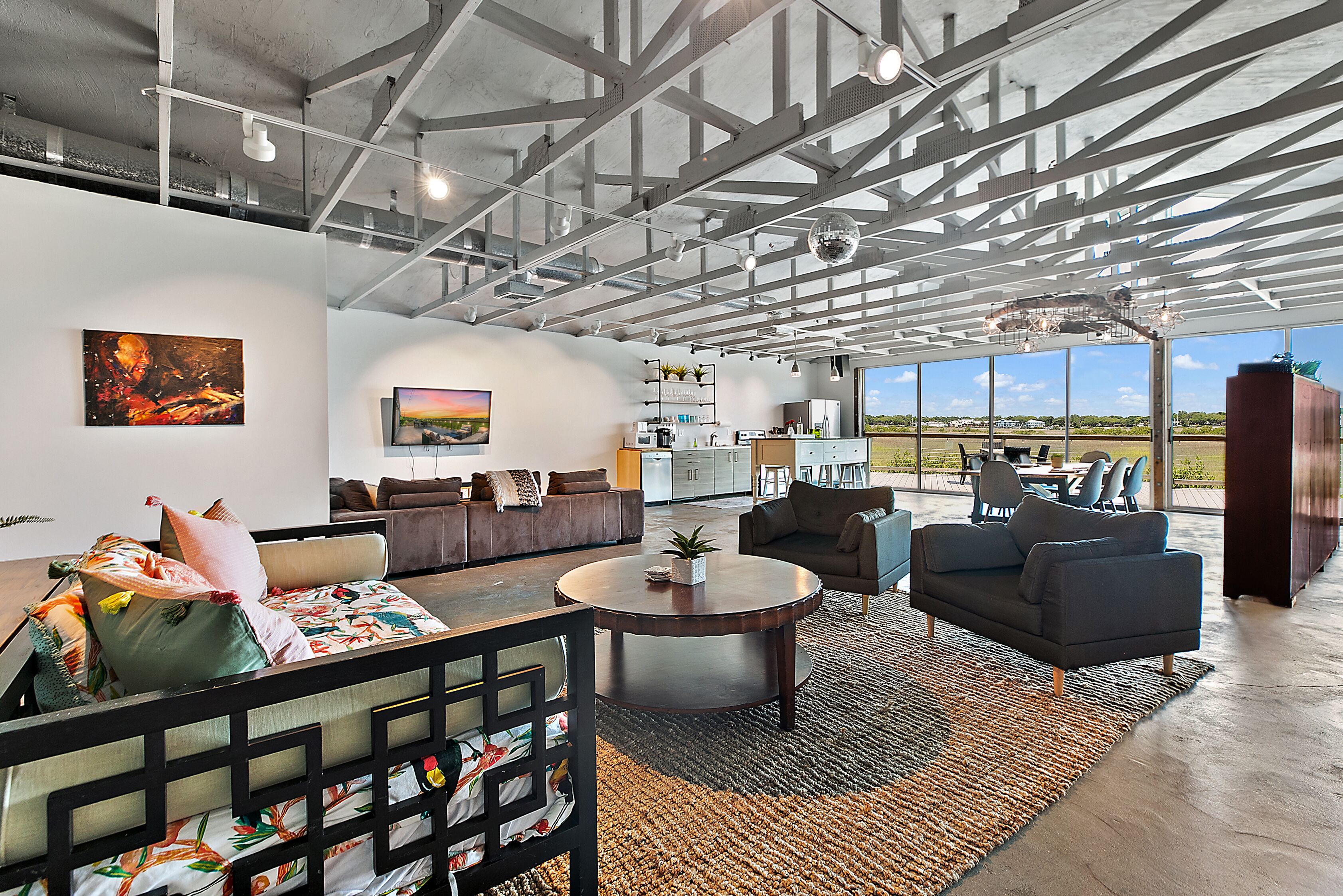 A spacious living area with a high ceiling, modern furniture, and large windows offering a view of the outdoors.
