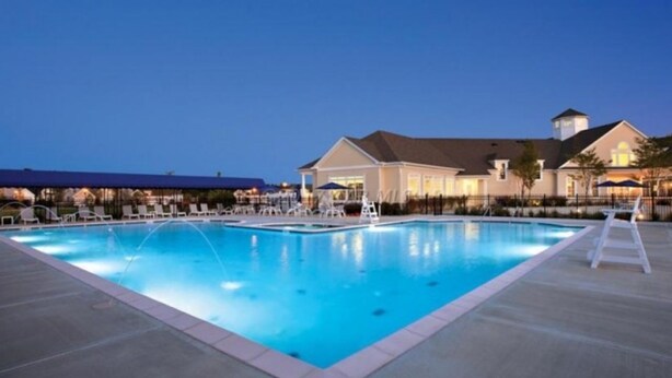A swimming pool with lounge chairs and a covered area, surrounded by buildings with a lighted facade. - Gorgeous Home in OC: Pools, Kayak, Fishing Pier, 5min to beach & Boardwalk, Golf (Berlin)