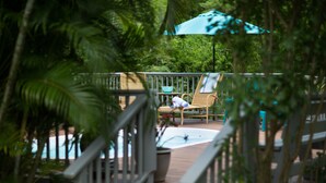 Une terrasse en bois avec une piscine, un fauteuil de relaxation et un parasol bleu.