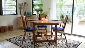 Un coin repas avec une table ronde, quatre chaises en bois dotées de coussins bleus, un vase avec des fleurs et une bougie.