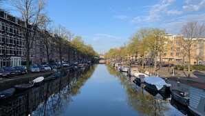 A canal lined with parked cars and boats, flanked by buildings and trees.