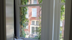A bedroom with a large window, a bed, and a view of a brick building.
