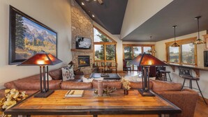 A spacious living room with a stone fireplace, leather sofas, and a large painting of a mountain landscape. - Slopeside Saddlewood: True Ski-in/Out, Private Hot Tub, Grill, Shuttle (Breckenridge)