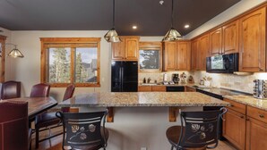 A modern kitchen with wooden cabinets, a granite countertop, and pendant lighting. - Slopeside Saddlewood: True Ski-in/Out, Private Hot Tub, Grill, Shuttle (Breckenridge)