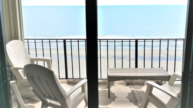 Un balcone con vista sulla spiaggia, due sedie bianche e un tavolino.