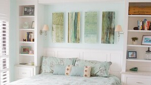 Una camera da letto con un letto, una panca, una ventola a soffitto, opere d'arte a parete e una libreria.