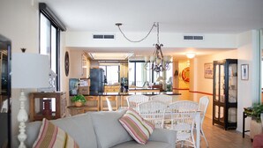 Un ampio soggiorno con divano, tavolo da pranzo e sedie. In secondo piano si vede una cucina con frigorifero e fornelli.