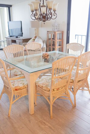 A dining area with a glass-top table surrounded by wicker chairs with floral cushions.