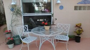 Een klein terras buiten met een ronde tafel en twee witte stoelen, omringd door potplanten.