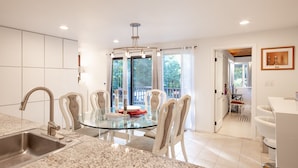 Una cocina moderna con una mesa de comedor de vidrio, armarios blancos y vistas al exterior.