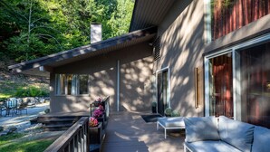 Una casa moderna con terraza de madera, mobiliario exterior y vistas a un bosque.