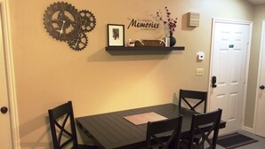 Comedor con una mesa y sillas negras, un reloj de pared, una estantería con adornos y una puerta.
